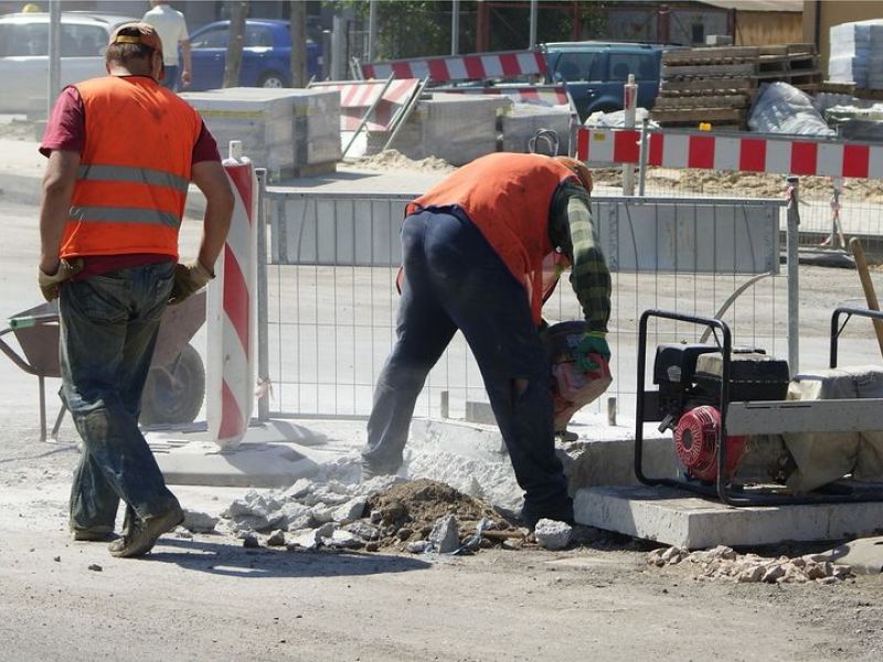 Na zdjęciu robotnicy pracujący przy remoncie drogi. W tle maszyny i narzędzia m.in. taczki.